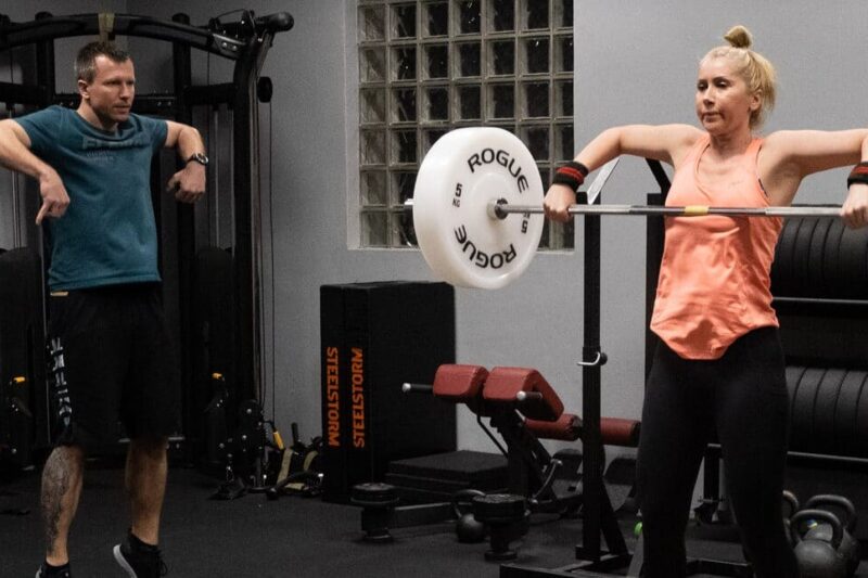 Trenerka wykonuje wyciąganie sztangi pod okiem trenera w studiu LIFT